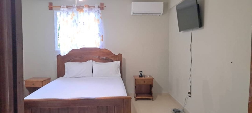 Guest bedroom with wooden bed, wall-mounted TV and air conditioning